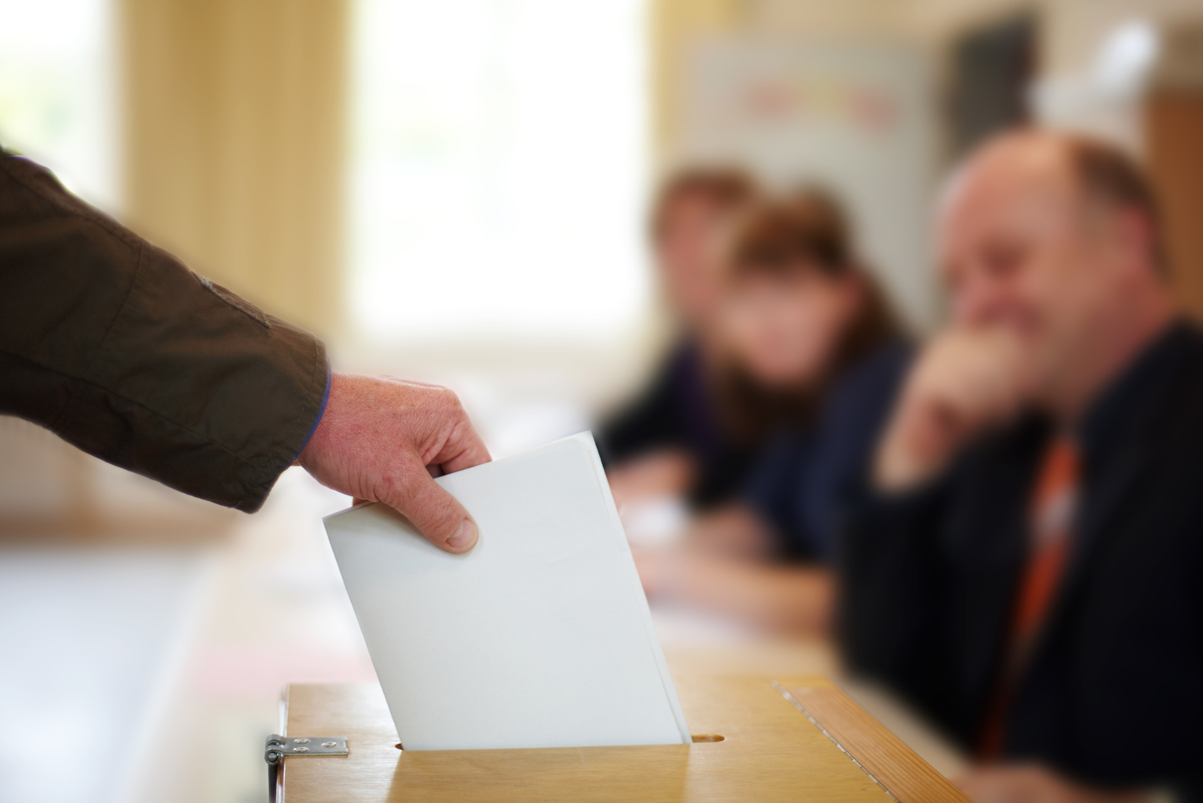 Męska ręka wrzucająca białą kartkę do urny wyborczej.