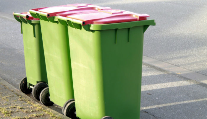 Trzy pojemniki na śmieci stojące przy krawężniku w kolorze zielonym z czerwoną klapą