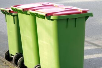 Trzy pojemniki na śmieci stojące przy krawężniku w kolorze zielonym z czerwoną klapą