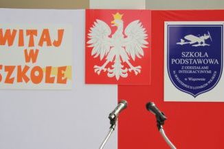 Biało-czerowna flaga, a na niej godło polski po środku, z lewej napis: Witaj w szkole, z prawej - tarcza