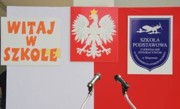 Biało-czerowna flaga, a na niej godło polski po środku, z lewej napis: Witaj w szkole, z prawej - tarcza