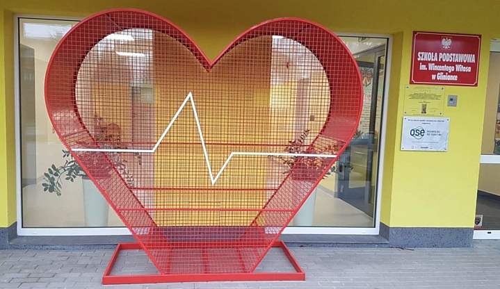 Czerwone, metalowe serce - pojemnik, do którego można wrzucać nakrętki stoi przed Szkołą Podstawową w Gliniance