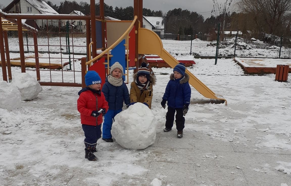 Czworo dzieci toczy kulę ze śniegu