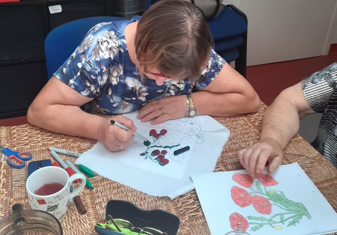 Seniorka maluje kwiaty na tkaninie