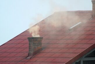 Bordowy dach. Z komina leci siwy dym.