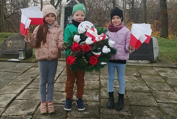 Dzieci z grupy Muchomorki z Gminnego Przedszkola im. Misia Uszatka w Wiązownie z biało-czerwonymi flagami i wiązanką kwiatów na kopcu w Wiązownie