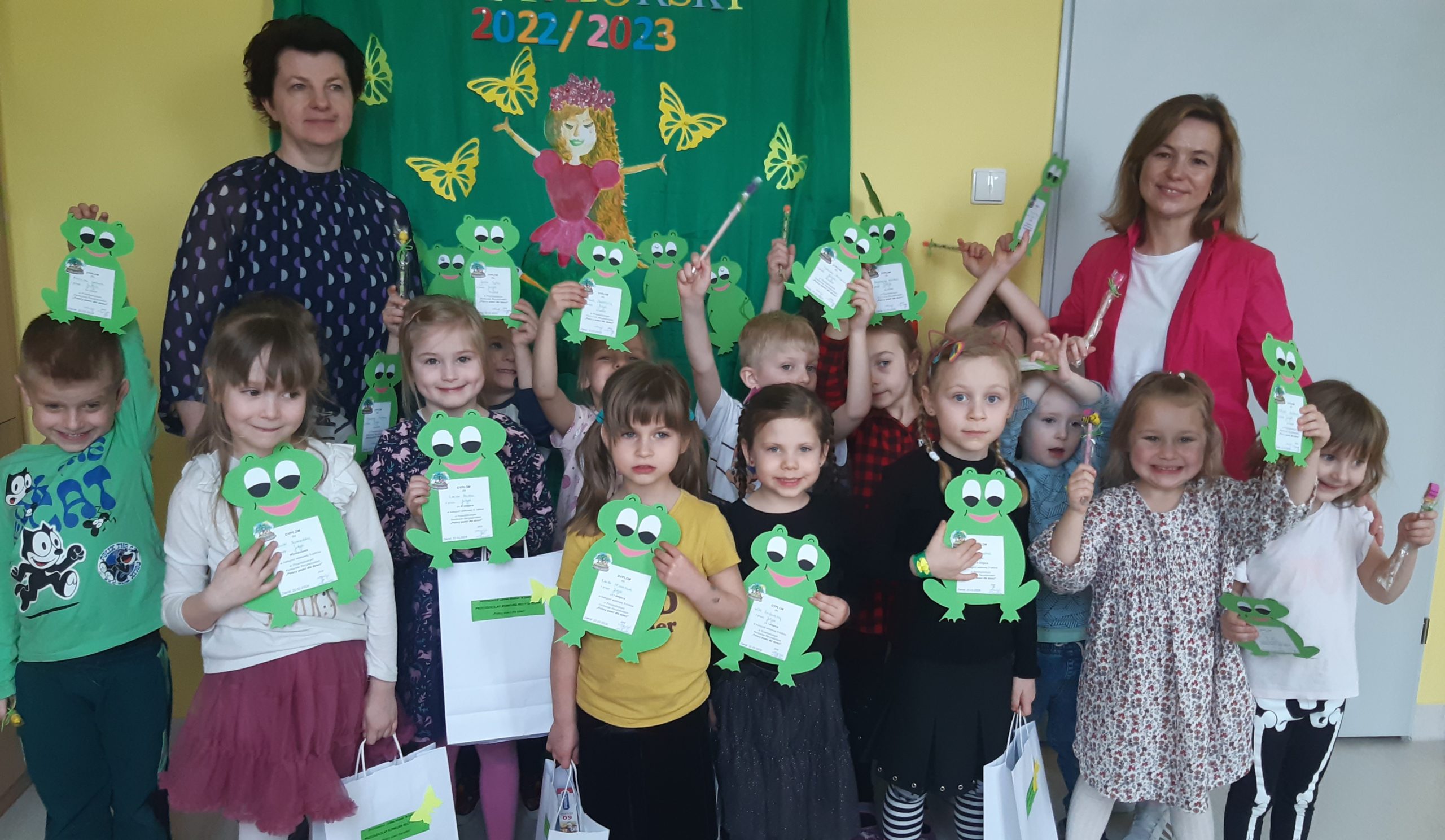 Przedszkole w Zakręcie. Przedszkolny Konkurs Recytatorski „Polscy poeci dla dzieci”. Dzieci prezentują dyplomy w kształcie zielonych żabek.