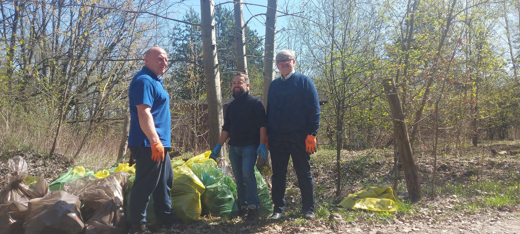 Coroczna akcja „Czyste sołectwo – moja wizytówka”. Trzech mężczyzn stoi w lesie przy workach wypełnionych śmieciami.