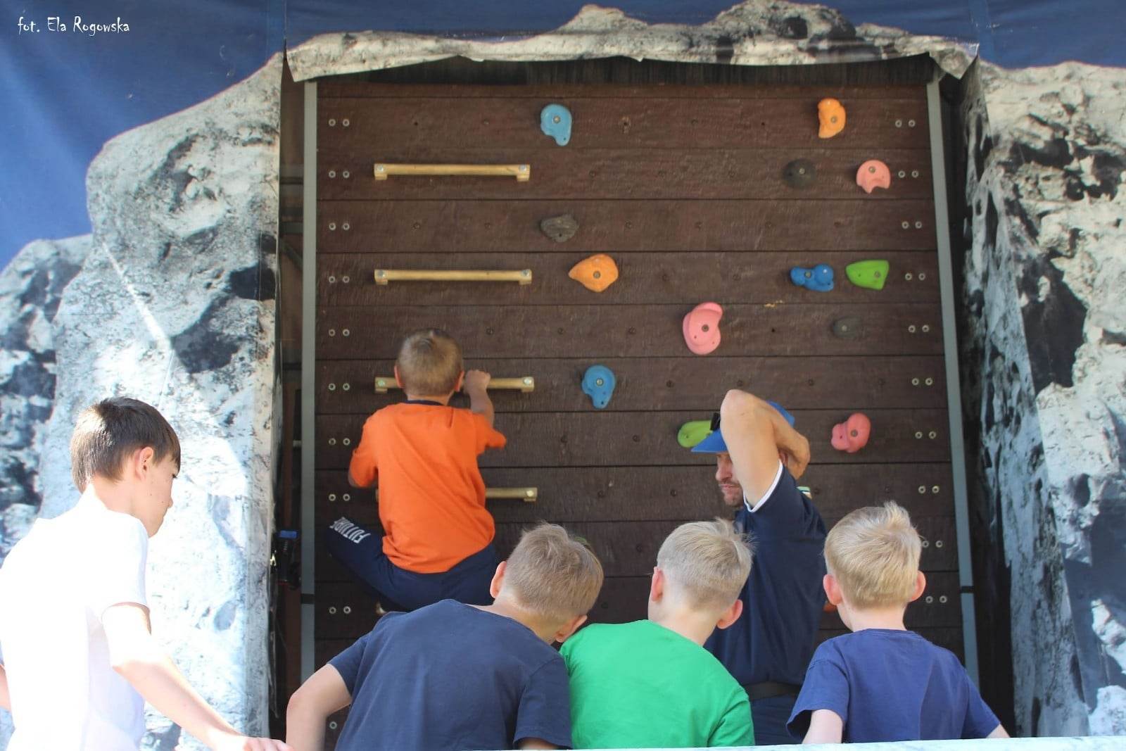 Instruktor i dzieci bawiące się na ściance wspinaczkowej.