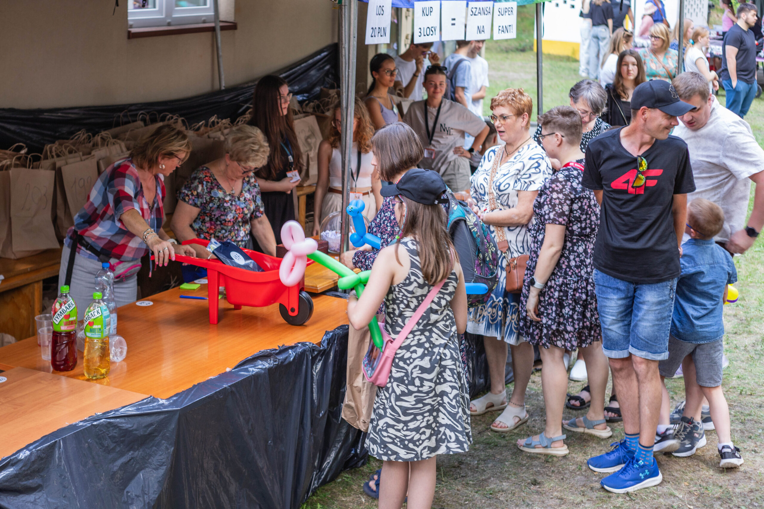 Kolejka ludzi do stoiska z loterią fantową.